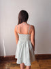 Woman wearing a light green dress with thin straps against a plain wall.