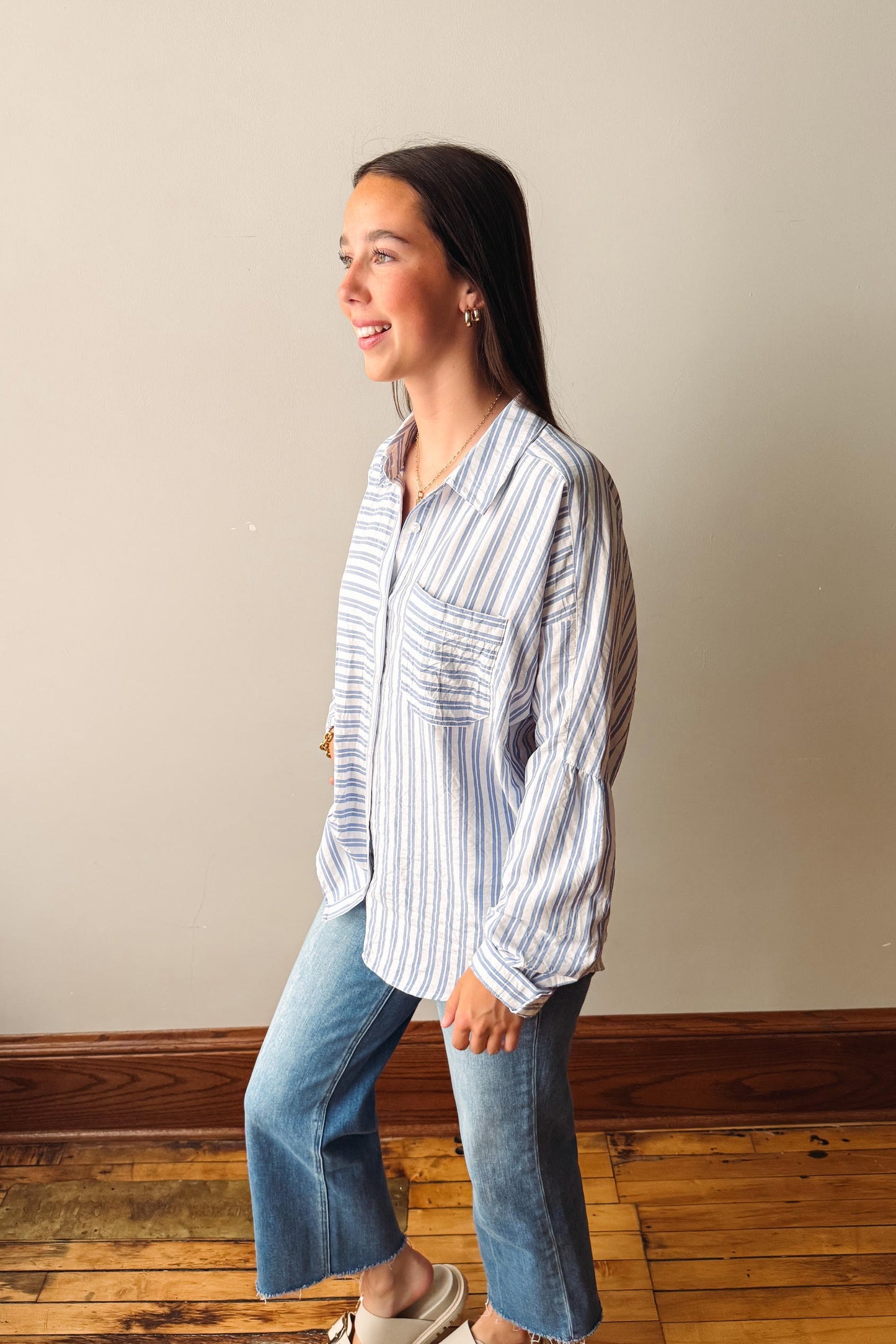Woman wearing a striped shirt and jeans standing against a plain wall.