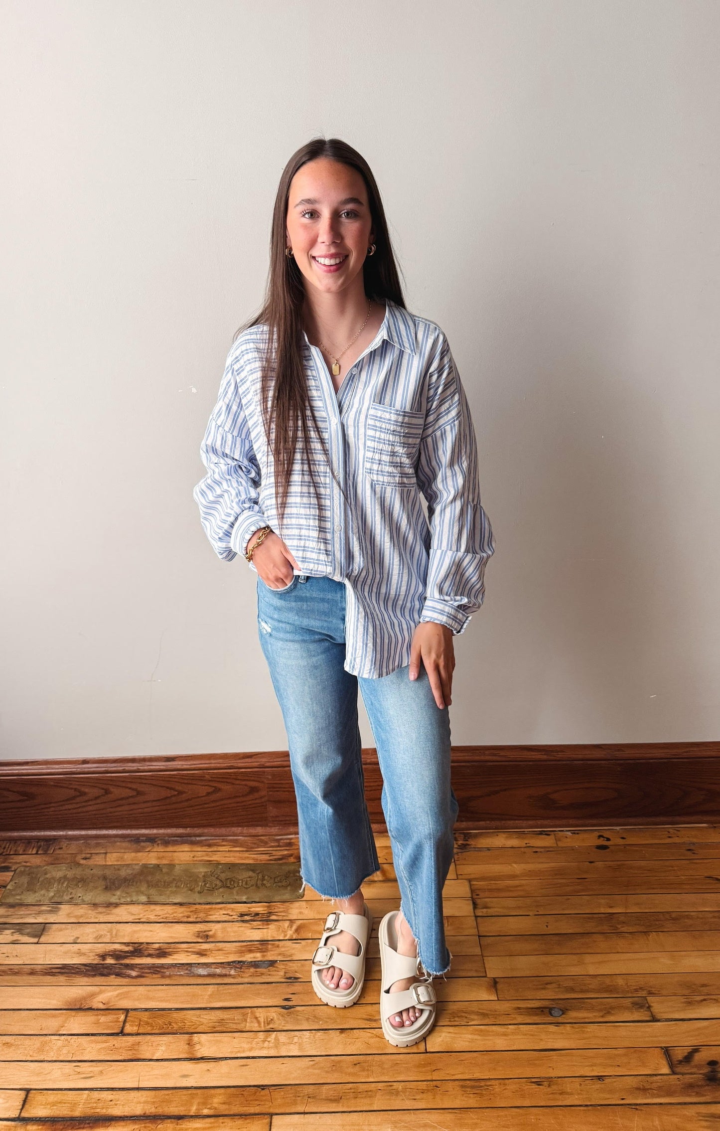 Woman wearing a striped shirt and jeans standing on a wooden floor.