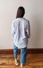 Person wearing a striped shirt and blue jeans standing on a wooden floor against a plain wall.