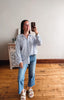 Woman taking a mirror selfie wearing a striped shirt and jeans in a room with wooden flooring.