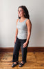 A woman modeling a light gray ribbed tank top and dark charcoal gray wide-leg jeans with black sandals, standing on a wooden floor against a plain off-white wall.