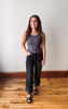 A woman modeling a dark gray ribbed tank top and black wide-leg cropped jeans with black sandals, standing on a wooden floor against a plain off-white wall.