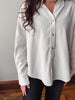 A woman wearing a cream-colored, long-sleeve button-down shirt with subtle vertical textured stripes, paired with black pants.