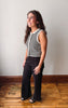 A woman modeling a sleeveless black and white striped top with white trim, paired with black wide-leg pants and black slide sandals, standing on a wooden floor against a plain light gray wall.