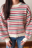 A person wearing a chunky knit sweater with horizontal stripes in cream, red, and navy blue, paired with blue jeans.