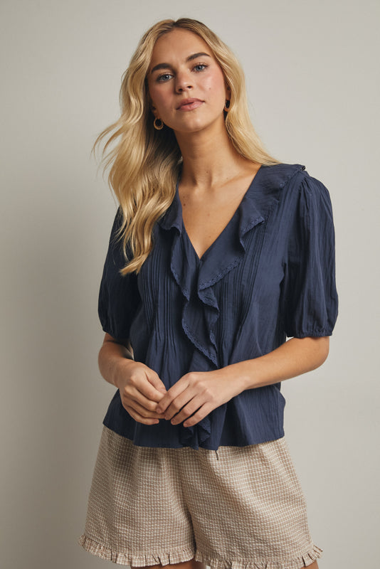 Woman wearing a navy blouse with puff sleeves and beige shorts against a neutral background