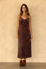 A woman modeling a dark brown velvet slip dress with a tonal floral jacquard pattern, paired with brown suede ankle boots, standing against a textured beige wall.