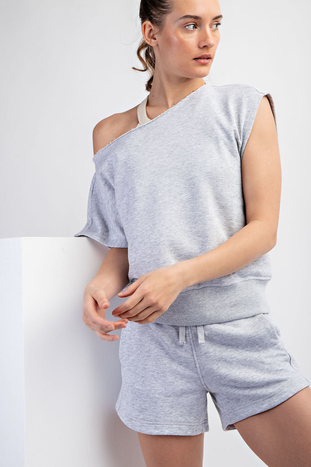 Woman wearing a gray off-shoulder top and shorts against a white background