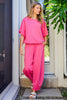 Woman wearing a bright pink outfit standing in front of a glass door with greenery around.