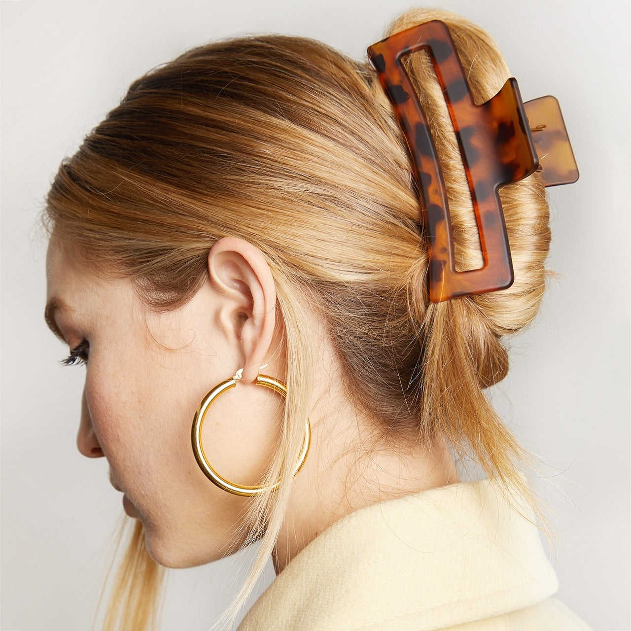 Woman with a bun held by a tortoiseshell hair clip, wearing gold hoop earrings.