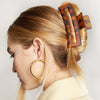 Woman with a bun held by a tortoiseshell hair clip, wearing gold hoop earrings.