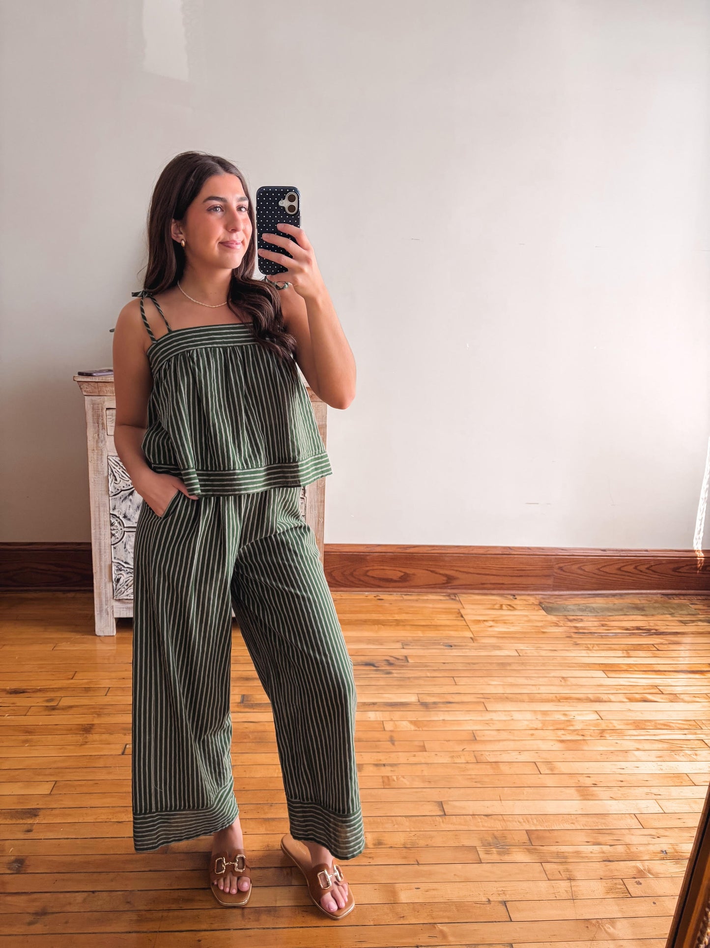 Woman taking a mirror selfie wearing a green striped jumpsuit in a room with wooden flooring.