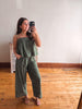 Woman taking a mirror selfie wearing a green striped jumpsuit in a room with wooden flooring.