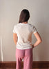 Person wearing a white t-shirt and pink pants standing against a plain wall.