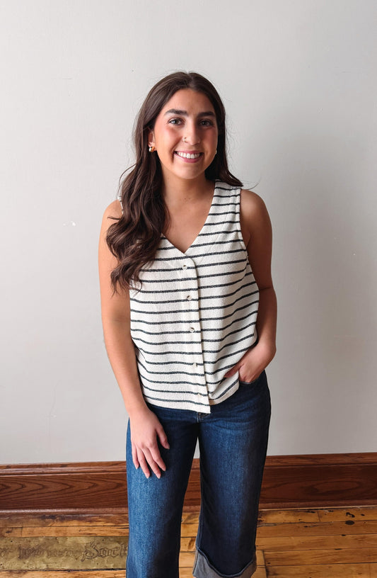 Woman wearing a striped sleeveless top and jeans standing against a plain wall.
