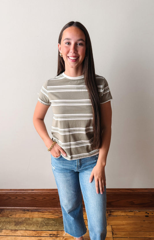 Woman wearing a striped shirt and jeans standing against a plain wall.