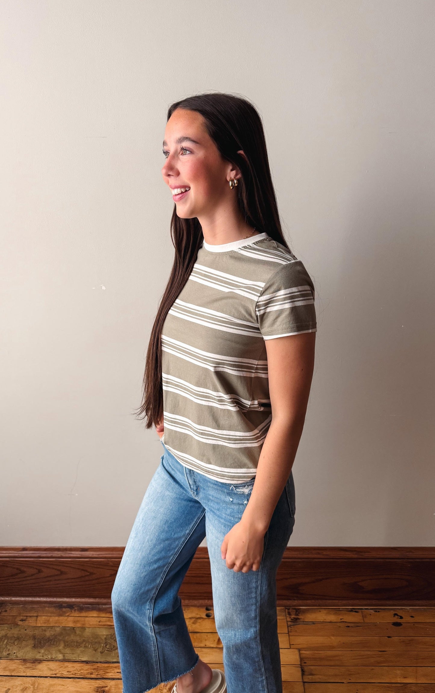 Woman wearing a striped shirt and jeans standing against a plain wall.