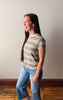 Woman wearing a striped shirt and jeans standing against a plain wall.