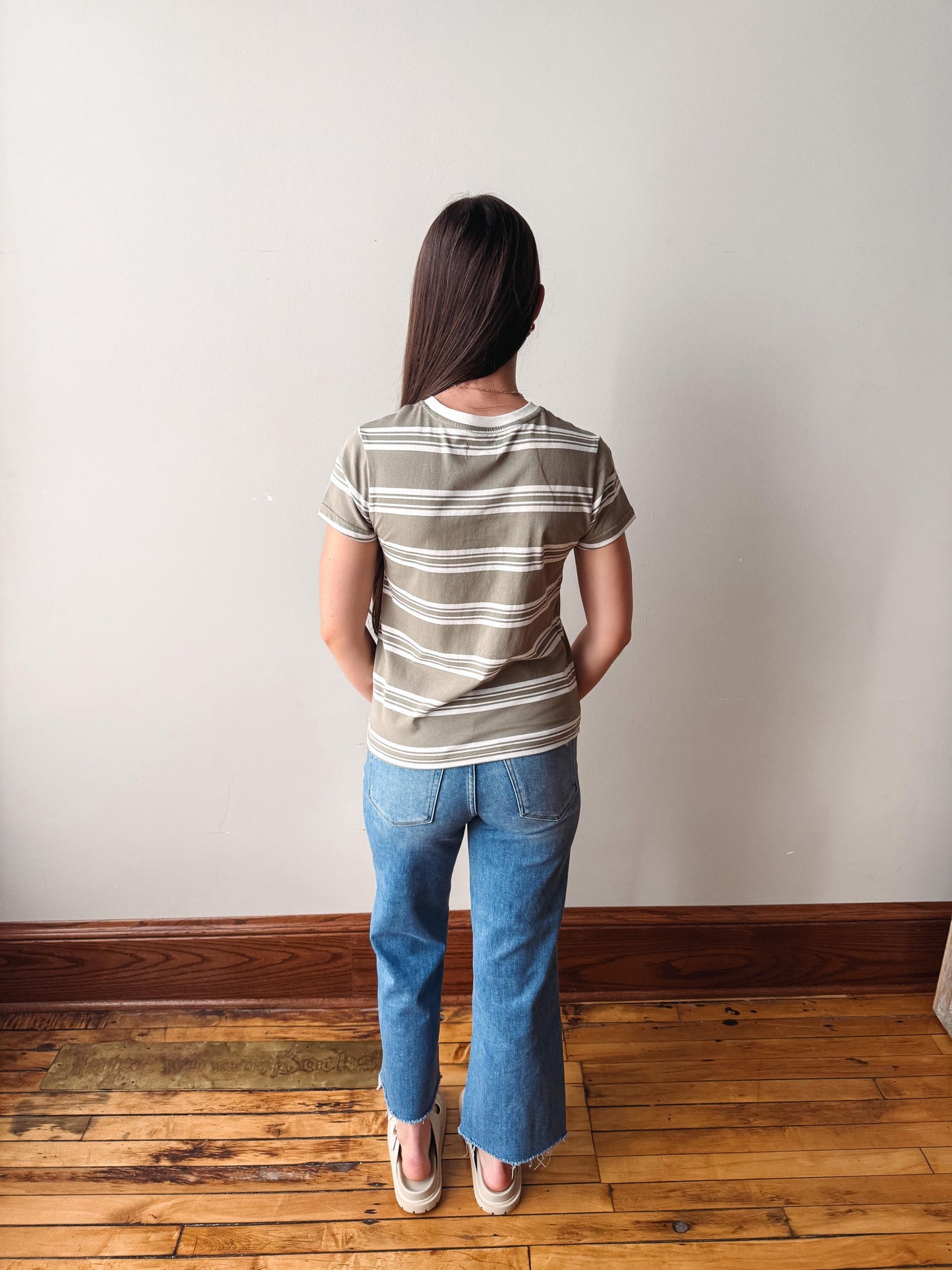 Person wearing a striped shirt and blue jeans standing against a plain wall.