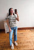 Woman taking a mirror selfie wearing a striped shirt and jeans in a room with wooden flooring.