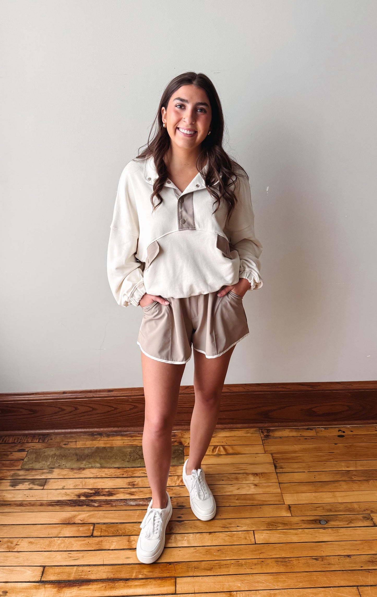 Woman wearing a white blouse and beige shorts standing on a wooden floor.