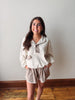 Woman wearing a beige outfit with a white wall background