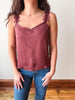A woman wearing a dusty rose crinkled camisole top with lace trim on the straps, paired with blue jeans, standing indoors against a plain wall.