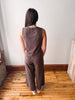 A woman viewed from behind wearing a matching sleeveless top and wide-leg pants set in a muted brown color, standing on a wooden floor against a plain wall.