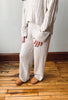 A person wearing a cream cable-knit sweater and matching wide-leg pants, standing on a wooden floor against a light wall.