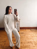 A woman takes a mirror selfie wearing a matching cream cable-knit sweater and wide-leg pants set, standing on a wooden floor against a white wall.