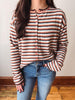 A woman wearing a fuzzy knit long-sleeve cardigan with horizontal stripes in rust orange, brown, and cream, paired with blue jeans.