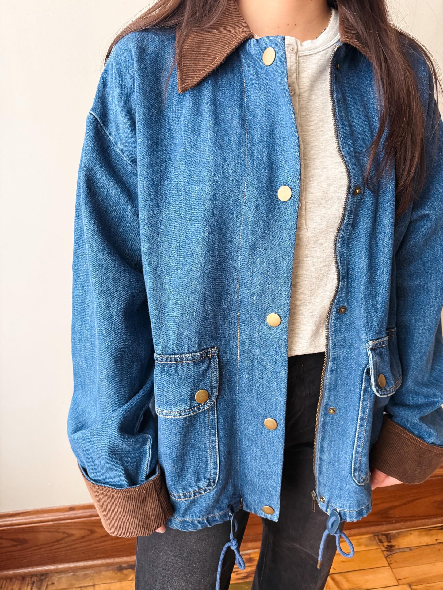 A person wearing a blue denim jacket with brown corduroy collar and cuffs, layered over a light gray shirt and dark pants.