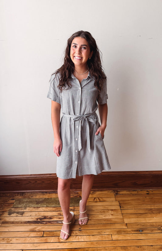 Woman wearing a checkered dress standing on a wooden floor with a white wall background