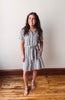 Woman wearing a checkered dress standing on a wooden floor with a white wall background