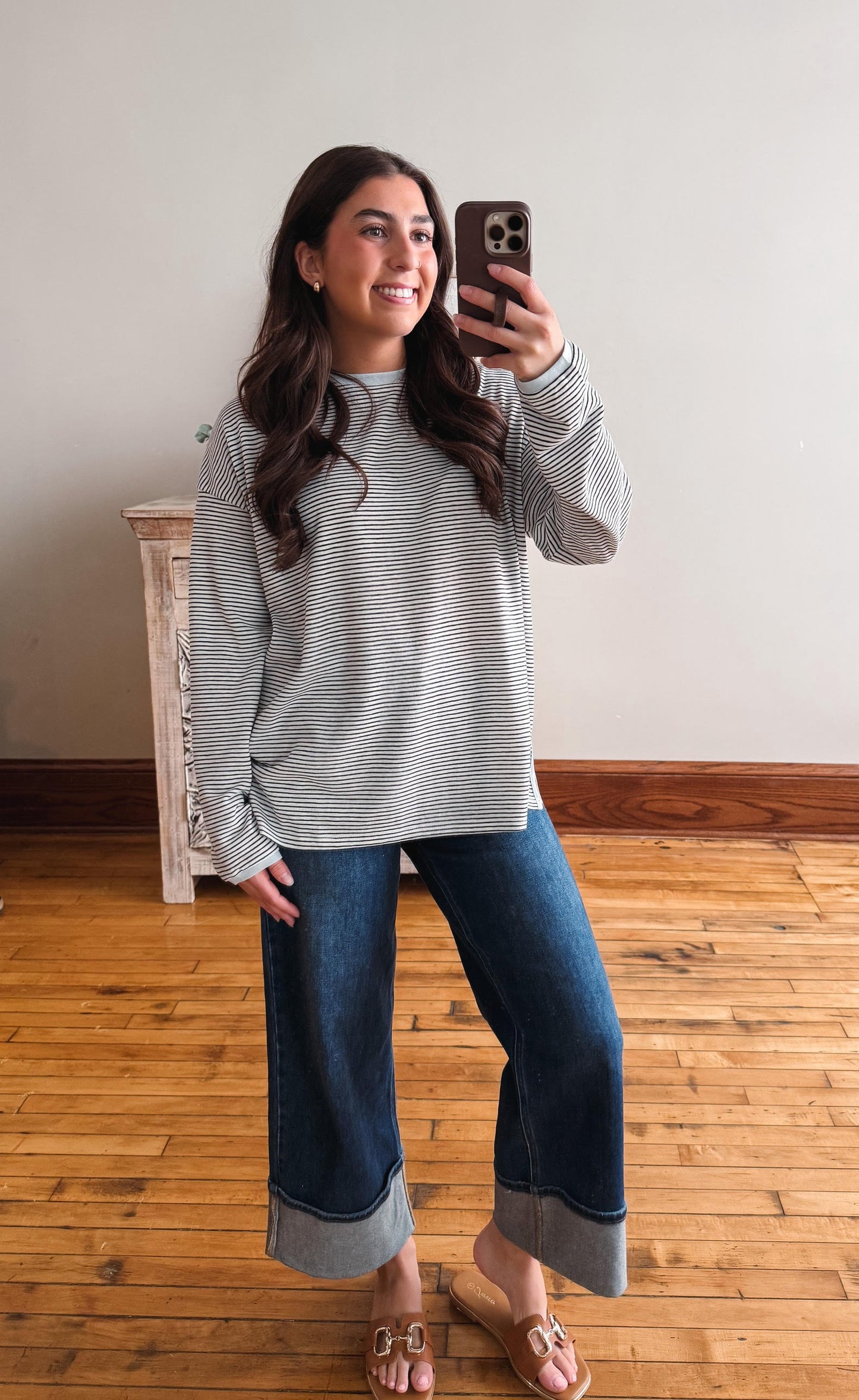 Woman taking a mirror selfie wearing a striped sweater and jeans on a wooden floor.