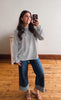 Woman taking a mirror selfie wearing a striped sweater and jeans on a wooden floor.