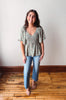 Woman wearing a floral blouse and jeans standing on a wooden floor with a white wall background