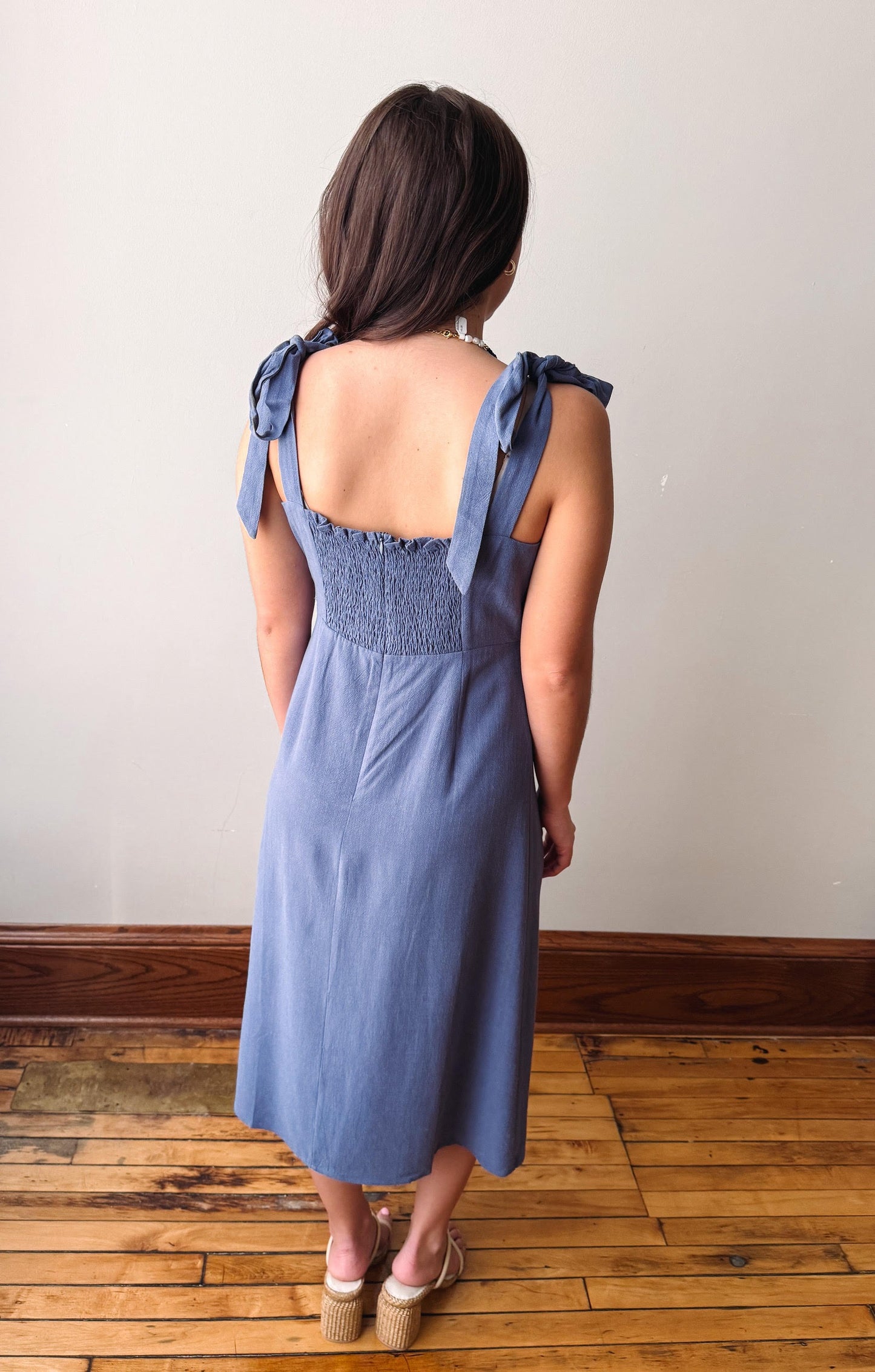 Woman wearing a blue dress with bow straps standing on a wooden floor.