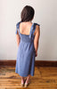 Woman wearing a blue dress with bow straps standing on a wooden floor.