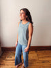 Woman wearing a light blue sleeveless top and jeans standing on a wooden floor.