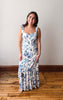 Woman wearing a floral dress standing on a wooden floor with a white wall background