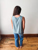 Person wearing a light blue sleeveless top and jeans standing against a white wall.