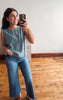 Woman taking a mirror selfie wearing a light blue sleeveless top and blue jeans.