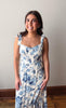 Woman wearing a floral dress standing against a plain wall.