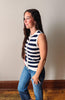 Woman wearing a navy and white striped sleeveless top and blue jeans against a plain wall.