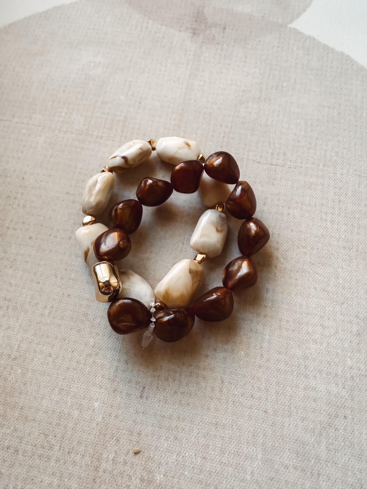 Beaded bracelet with brown and white beads on a beige fabric background