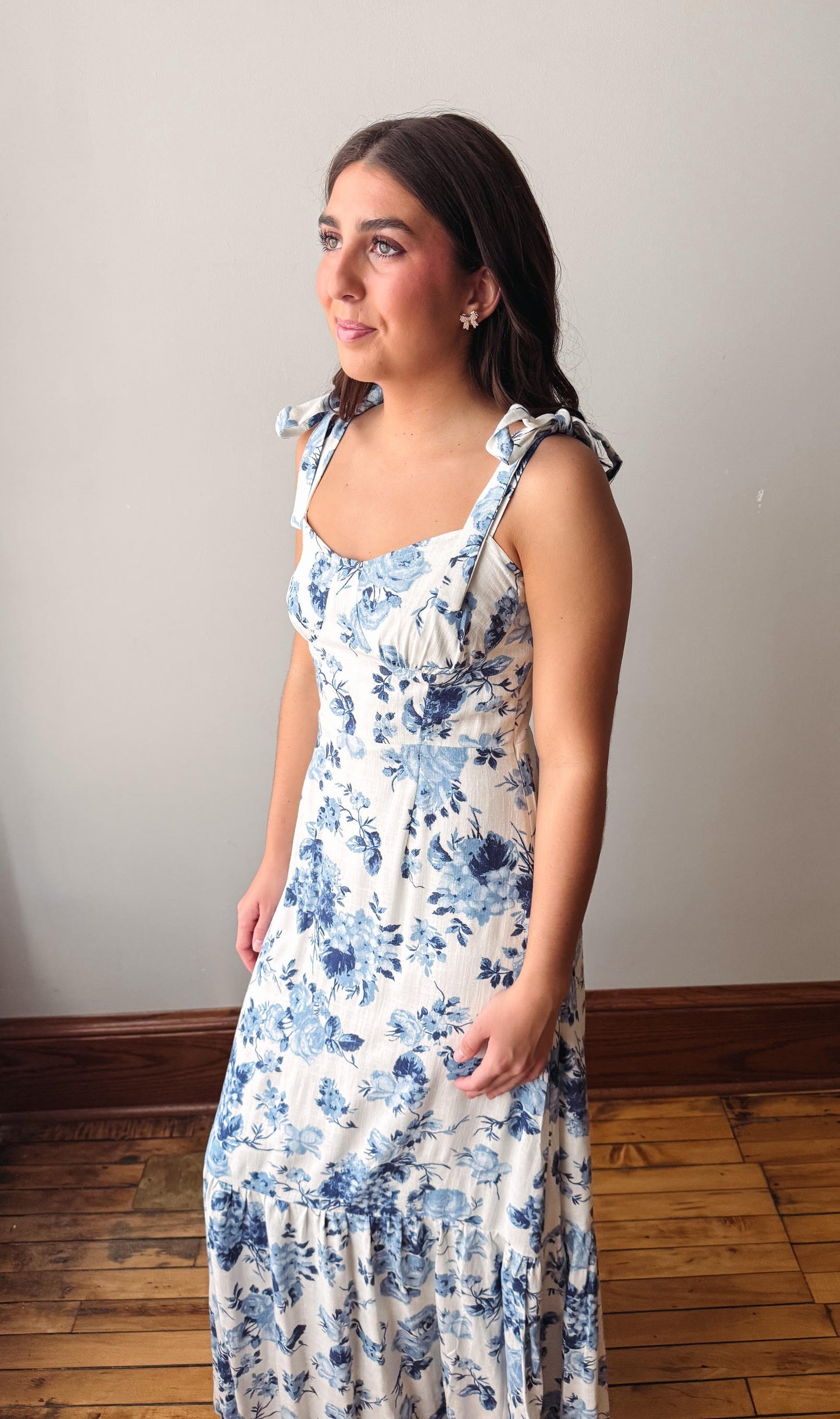 Woman wearing a floral dress standing against a plain wall.