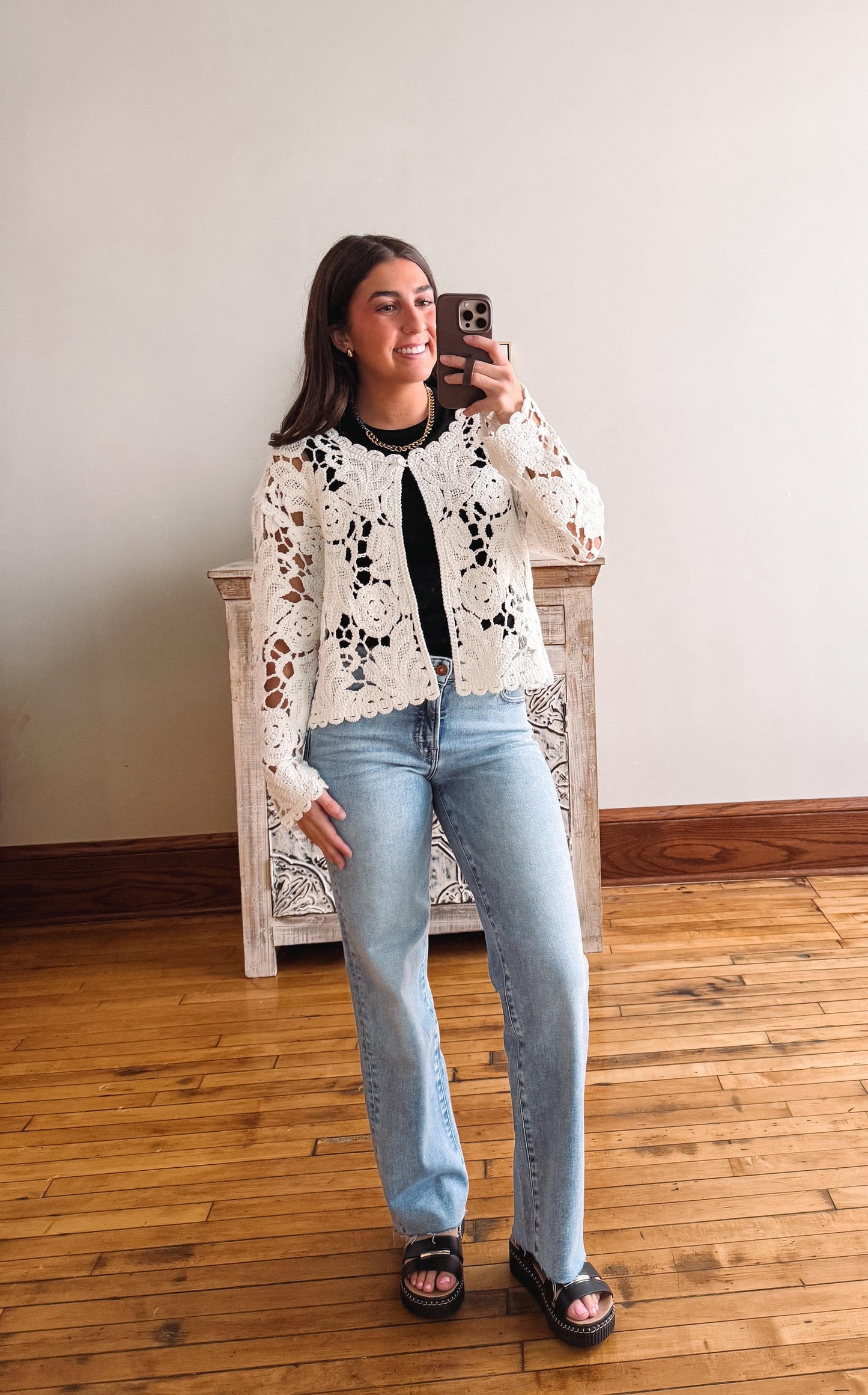 Woman taking a mirror selfie wearing a floral lace top and light blue jeans.
