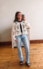 Woman taking a mirror selfie wearing a floral lace top and light blue jeans.
